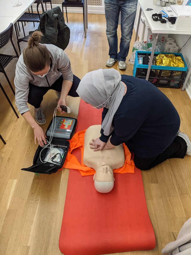 Tumma-asuinen henkilö harjoittelemassa paineluelvytystä ensiapukurssilla. Tumma-asuinen henkilö harjoittelemassa paineluelvytystä ensiapukurssilla.